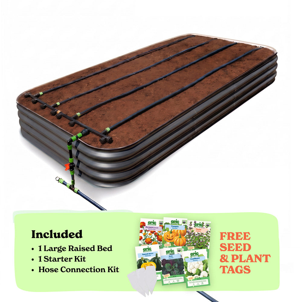 A raised garden bed in slate gray color filled with soil, shown with drip irrigation tubing laid across the top. A light green promotional banner at the bottom lists included items: 1 15-inch tall large raised bed, 1 starter kit, and hose connection kit, with a small image of seed packets and the text 'Free Seed & Plant Tags'.