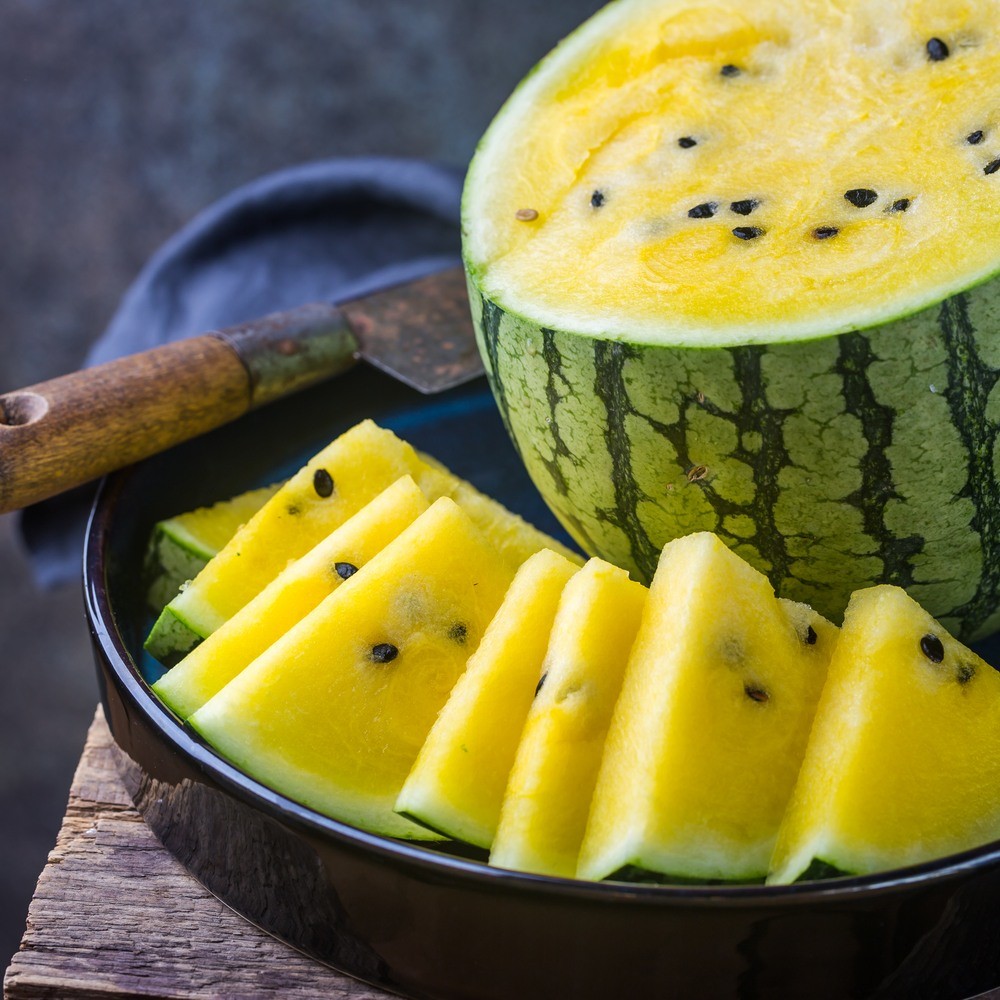Yellow Cream of Saskatchewan Watermelon sliced on a dark plate with a knife on a rustic wooden surface.