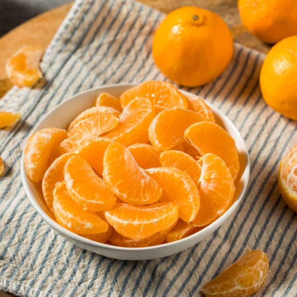 Bowl of peeled California Honey mandarin segments next to whole mandarins on a striped cloth.