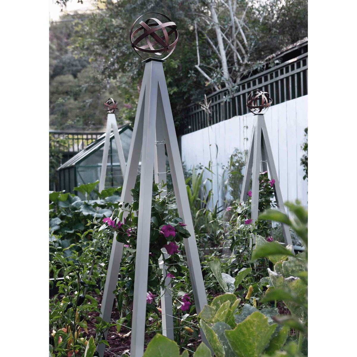 Zinc pyramid-shaped metal Akoris Garden Obelisk Large trellises with bronze sphere finials set among lush green foliage and purple flowering plants
