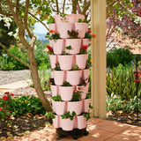Seven-tier terracotta-pink GreenStalk Vertical Planter Basketweave filled with flowering plants and greens, set on a rolling base on a tiled patio next to a tree and garden bed.