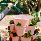 Watering the top reservoir of a pink GreenStalk Vertical Planter Basketweave with a hose.