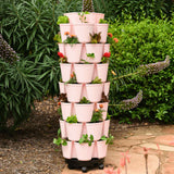 Seven-tier soft pink GreenStalk Vertical Planter Basketweave filled with mixed leafy greens and small flowering plants, set on a rolling base in a garden setting outdoors.