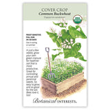 Seed packet for Common Buckwheat cover crop showing an illustration of heart-shaped green leaves with clusters of small white flowers above a raised garden bed densely filled with the growing crop and a garden fork stuck in the soil, alongside text noting it's frost sensitive, needs full sun, matures in 30-40 days, and describes its use as a soil-enriching green manure that suppresses weeds and attracts bees.