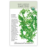 Seed packet for organic Baby Greens Arugula (Rocket), featuring a detailed illustration of deeply lobed, jagged green leaves, with printed text noting 20–28 day germination, indoor sowing instructions, and a description of its peppery flavor and nutritional benefits.