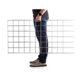 Side profile of a person carrying a flat, rectangular metal grid panel for Folding A-Frame Trellis Support For Plants.