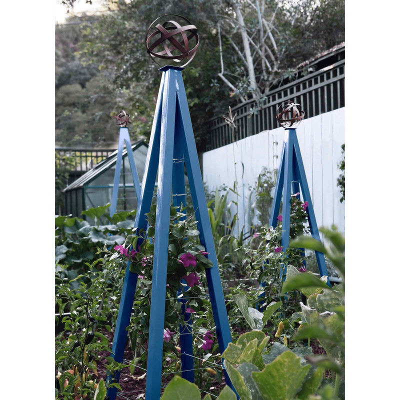 Blue pyramid-shaped metal Akoris Garden Obelisk Large trellises with bronze sphere finials set among lush green foliage and purple flowering plants
