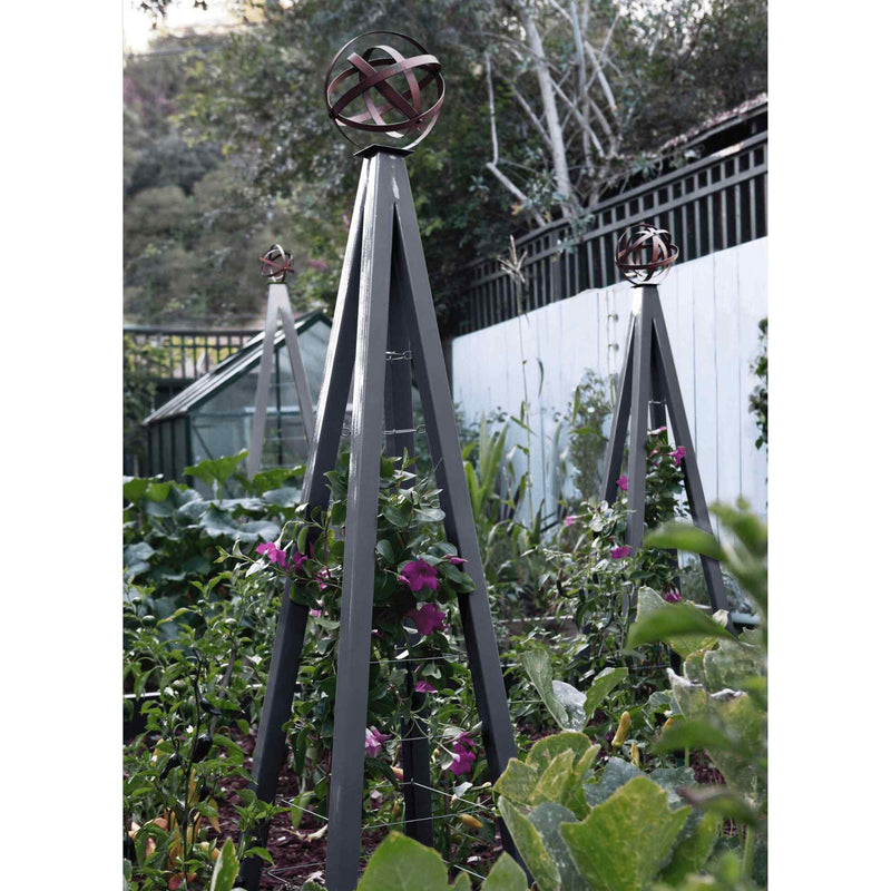 Charcoal pyramid-shaped metal Akoris Garden Obelisk Large trellises with bronze sphere finials set among lush green foliage and purple flowering plants