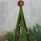 Olive green metal A-frame Bird Cafe with Trellis topped with a circular oxide steel bird feeder, set against a concrete wall with rosemary plants at the base