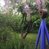 Rust-finished A-frame Bird Cafe with Trellis topped with a circular bird feeder, surrounded by green shrubs and orange flowering vines