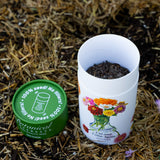 Open Botanical Interests Cut and Come Again Zinnia seed shaker tube next to its green lid on straw mulch.
