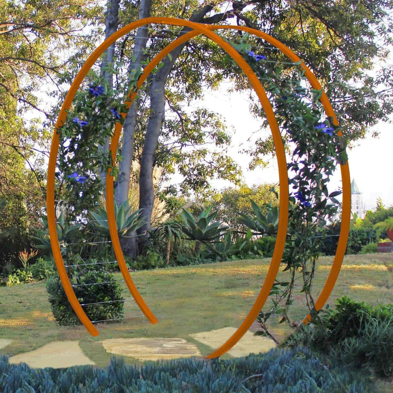 Bright orange circular metal Gracie Modern Arbor forming an arched gateway over a grassy path in a garden with trees and foliage