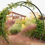 Olive green circular metal Gracie Modern Arbor forming a garden archway over a path, with a wooden greenhouse in the background,