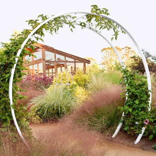 White metal circular Gracie Modern Arbor forming a dramatic entryway in a garden surrounded by ornamental grasses and flowering shrubs