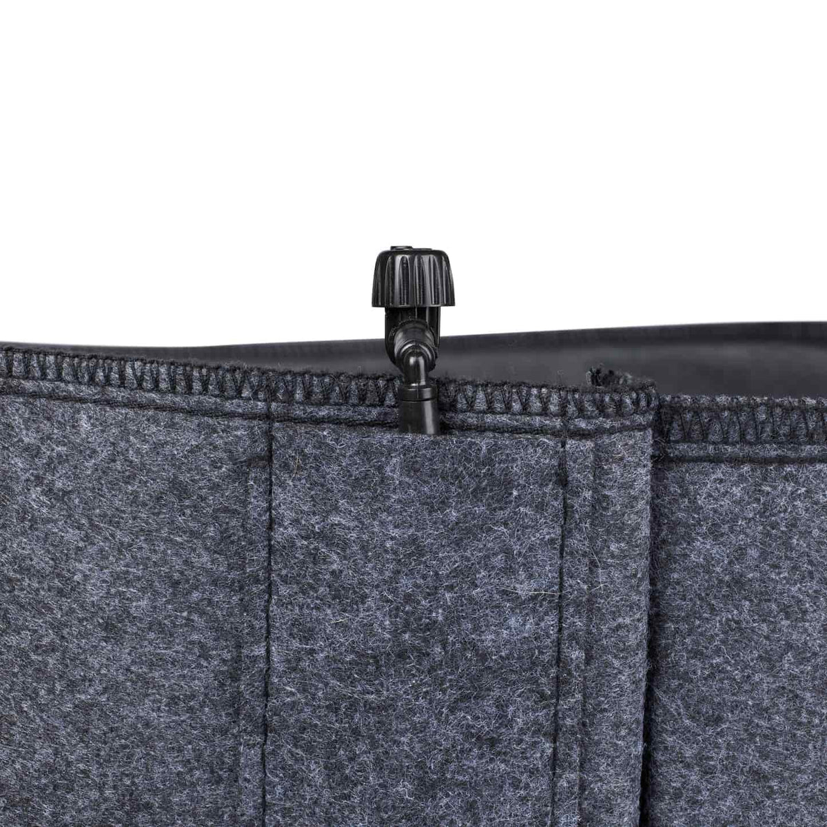 Close-up of a grey felt grow bag's stitched rim, showing a small black plastic irrigation valve fitted into the top seam for connecting a drip watering line.