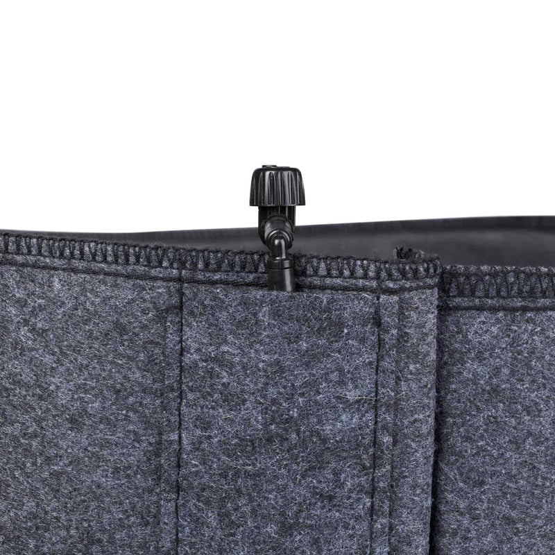 Close-up of a grey felt grow bag's stitched rim, showing a small black plastic irrigation valve fitted into the top seam for connecting a drip watering line.