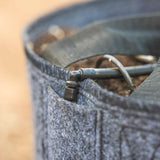 Close-up of a grey felt grow bag filled with soil, showing a small black irrigation fitting and curved drip tubing threaded over the rim.