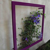 Purple square metal Ina Wall Trellis mounted on a gray wall with purple clematis flowers climbing through the wire grid