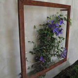 Zinc square metal Ina Wall Trellis mounted on a gray wall with purple clematis flowers climbing through the wire grid