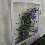 Silver square metal Ina Wall Trellis mounted on a gray wall with purple clematis flowers climbing through the wire grid