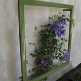 Olive green square metal Ina Wall Trellis mounted on a gray wall with purple clematis flowers climbing through the wire grid