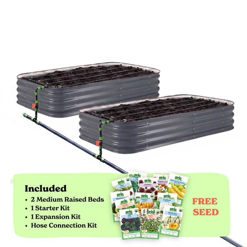 Two slate gray corrugated raised garden beds with soil inside, connected by a black hose of the epic irrigation system on a white background. A light green banner at the bottom lists included items: 2 15-inch tall medium raised beds, 1 starter kit, 1 expansion kit, and hose connection kit, with a small seed packet collage and the words 'FREE SEED'.