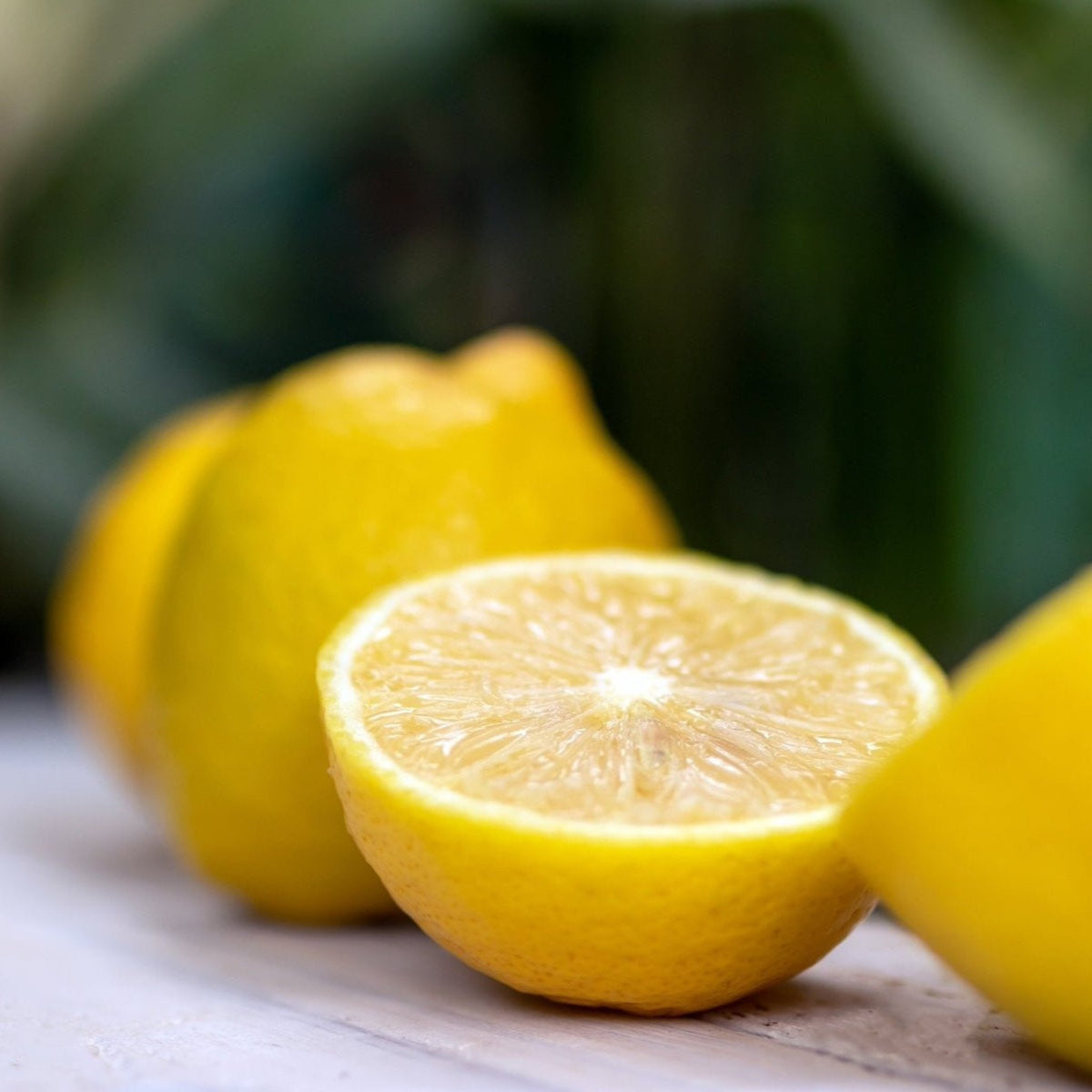 Close-up of a halved juicy Lisbon lemon with whole lemons on a wooden surface.