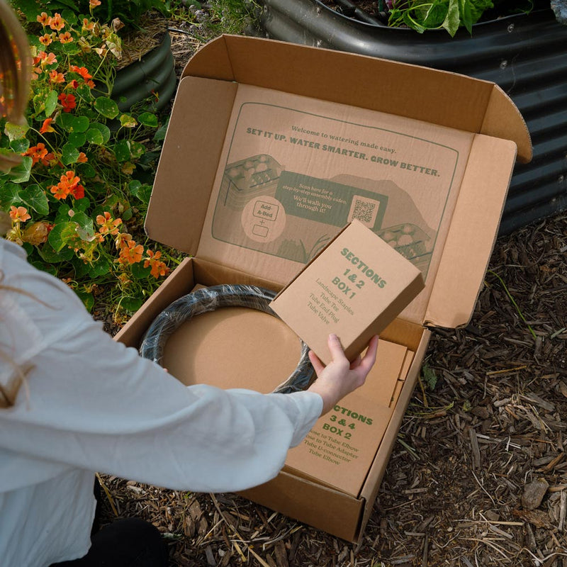 Person opening a cardboard box with the epic gardening irrigation system in an outdoor setting.