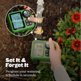Hand holding a green digital garden irrigation timer with plants in the background