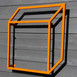 Bright orange cubic steel Pablo Wall Trellis mounted on a gray wooden wall, casting a sharp geometric shadow
