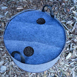 2-hole Plantable Fabric Cover fitted over a gray felt grow bag filled with soil outdoors on wood chips.