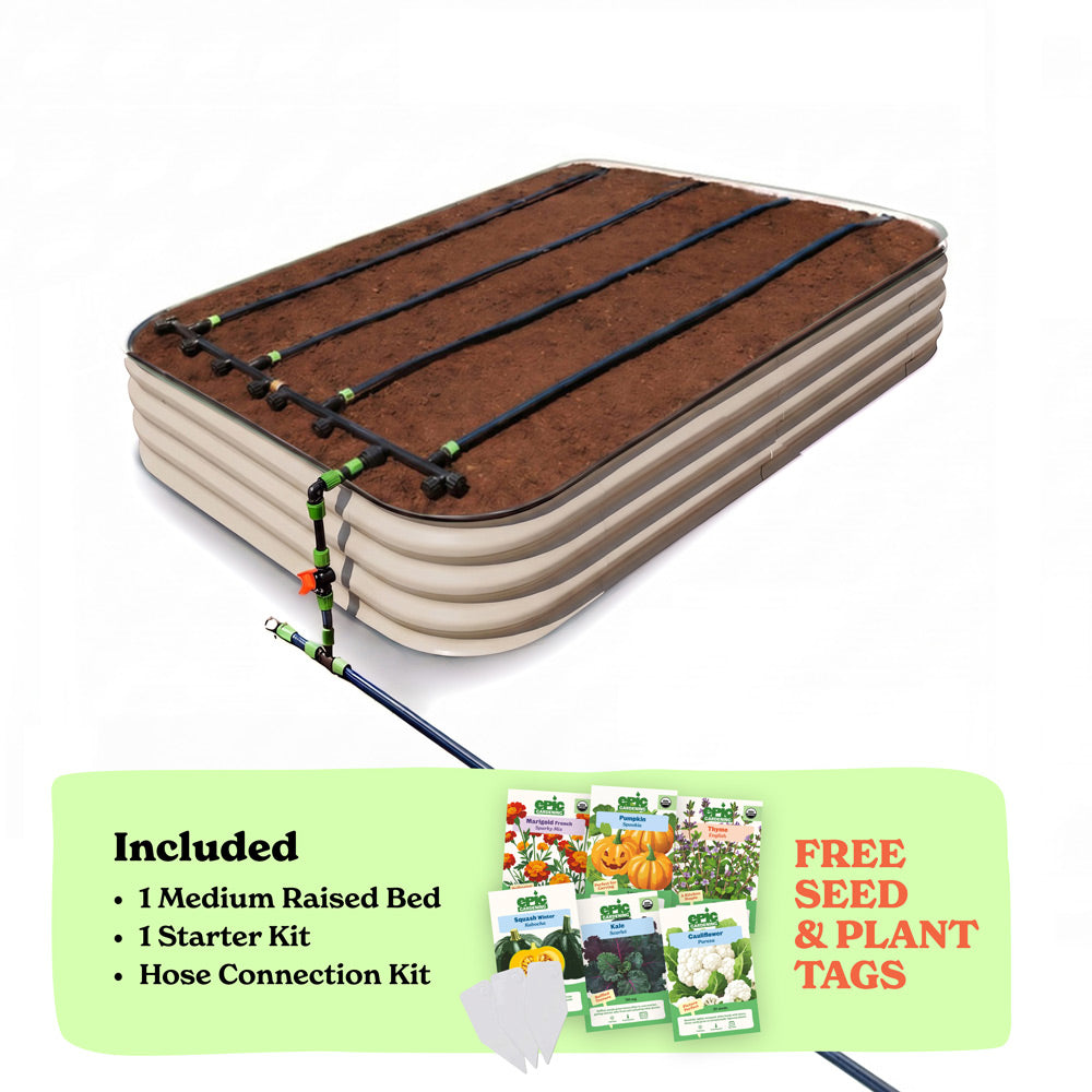A raised garden bed in light clay color filled with soil, shown with drip irrigation tubing laid across the top. A light green promotional banner at the bottom lists included items: 1 15-inch tall medium raised bed, 1 starter kit, and hose connection kit, with a small image of seed packets and the text 'Free Seed & Plant Tags'.