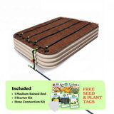 A raised garden bed in light clay color filled with soil, shown with drip irrigation tubing laid across the top. A light green promotional banner at the bottom lists included items: 1 15-inch tall medium raised bed, 1 starter kit, and hose connection kit, with a small image of seed packets and the text 'Free Seed & Plant Tags'.