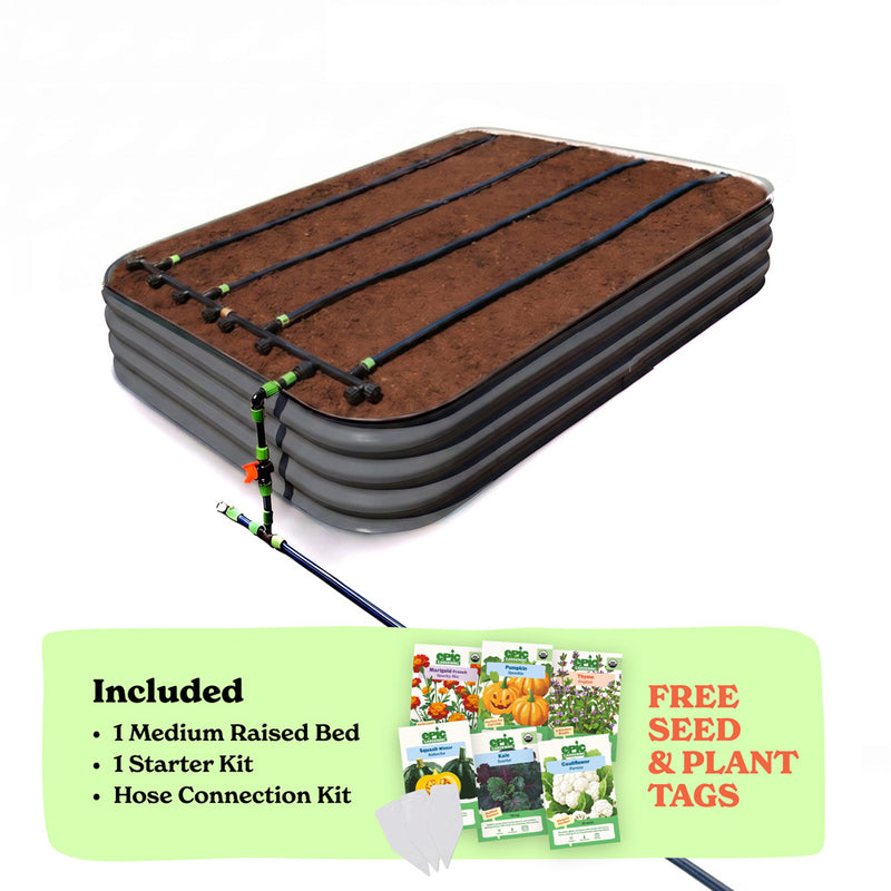 A raised garden bed in slate gray color filled with soil, shown with drip irrigation tubing laid across the top. A light green promotional banner at the bottom lists included items: 1 15-inch tall medium raised bed, 1 starter kit, and hose connection kit, with a small image of seed packets and the text 'Free Seed & Plant Tags'.