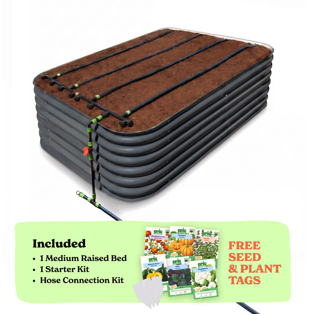 A raised garden bed in slate gray color filled with soil, shown with drip irrigation tubing laid across the top. A light green promotional banner at the bottom lists included items: 1 29-inch tall medium raised bed, 1 starter kit, and hose connection kit, with a small image of seed packets and the text 'Free Seed & Plant Tags'.