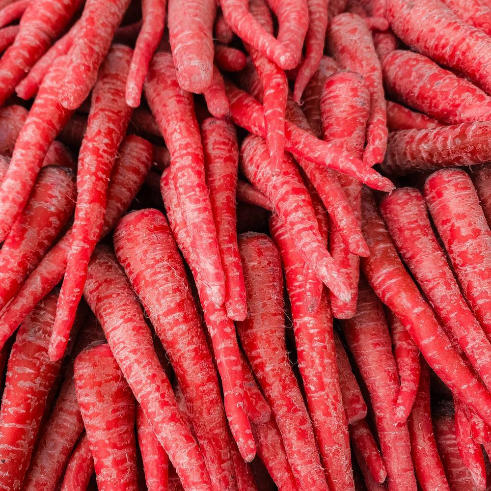 Close-up of freshly harvested Atomic Red carrots piled together, their deep red skin showing fine root hairs and pale streaking along the tapered roots.