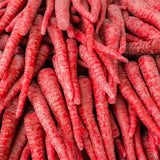 Close-up of freshly harvested Atomic Red carrots piled together, their deep red skin showing fine root hairs and pale streaking along the tapered roots.