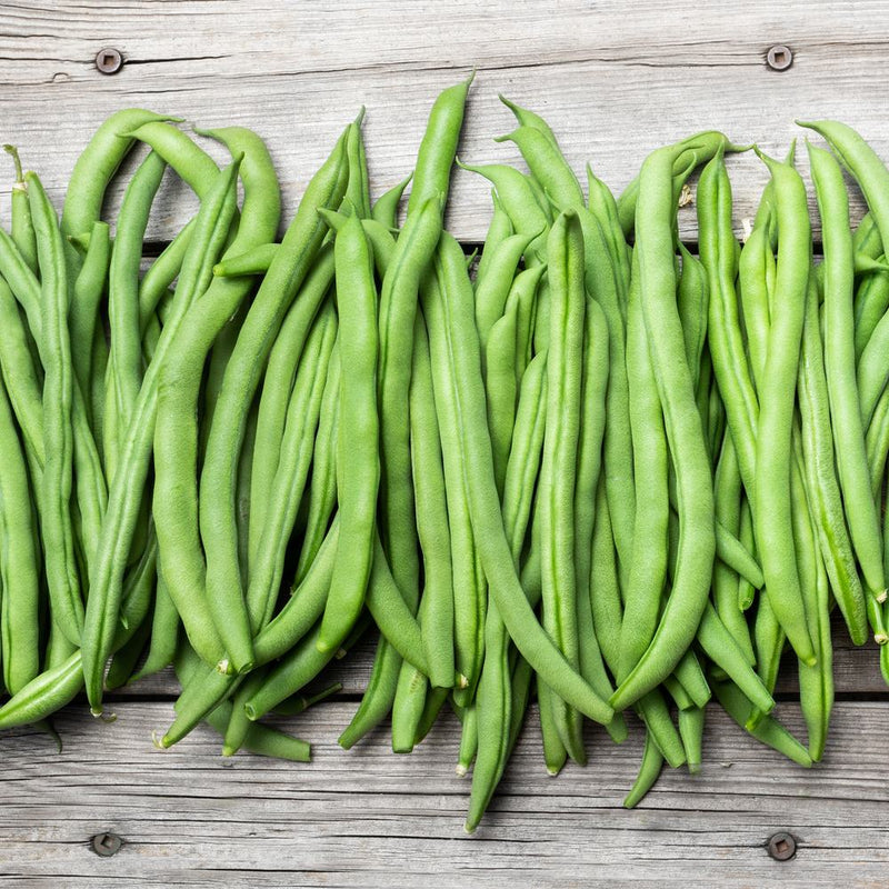 Freshly harvested long green bean pods arranged side by side on a rustic wooden surface