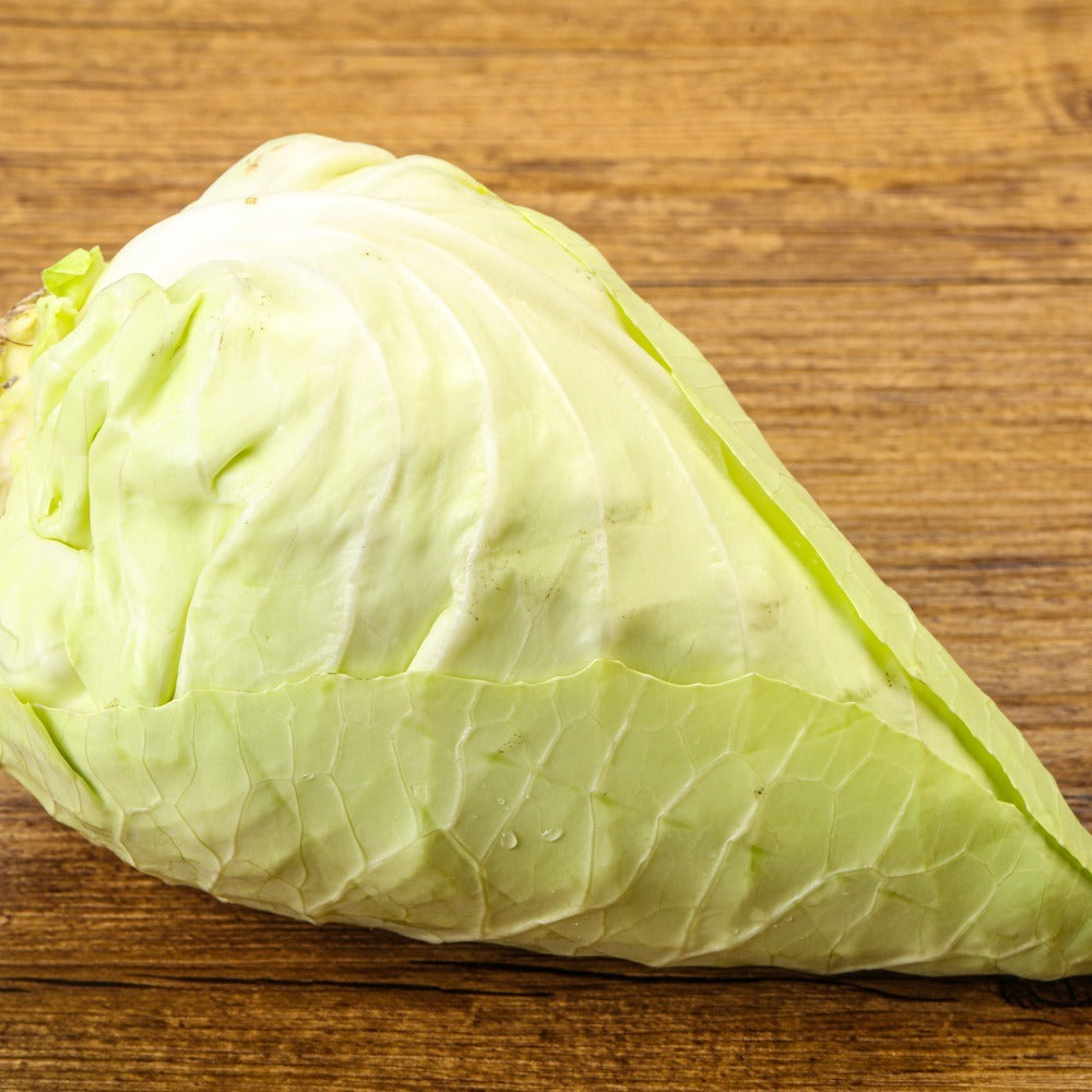 Pointed, cone-shaped Caraflex cabbage head with pale green, tightly wrapped leaves showing smooth veining, resting on a wooden surface.