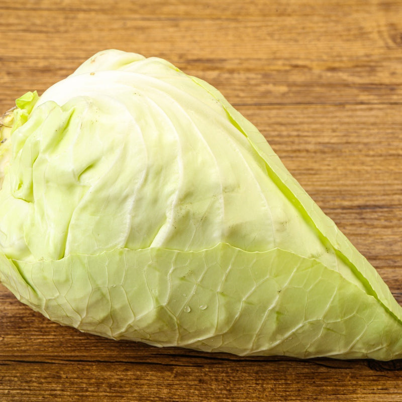 Pointed, cone-shaped Caraflex cabbage head with pale green, tightly wrapped leaves showing smooth veining, resting on a wooden surface.