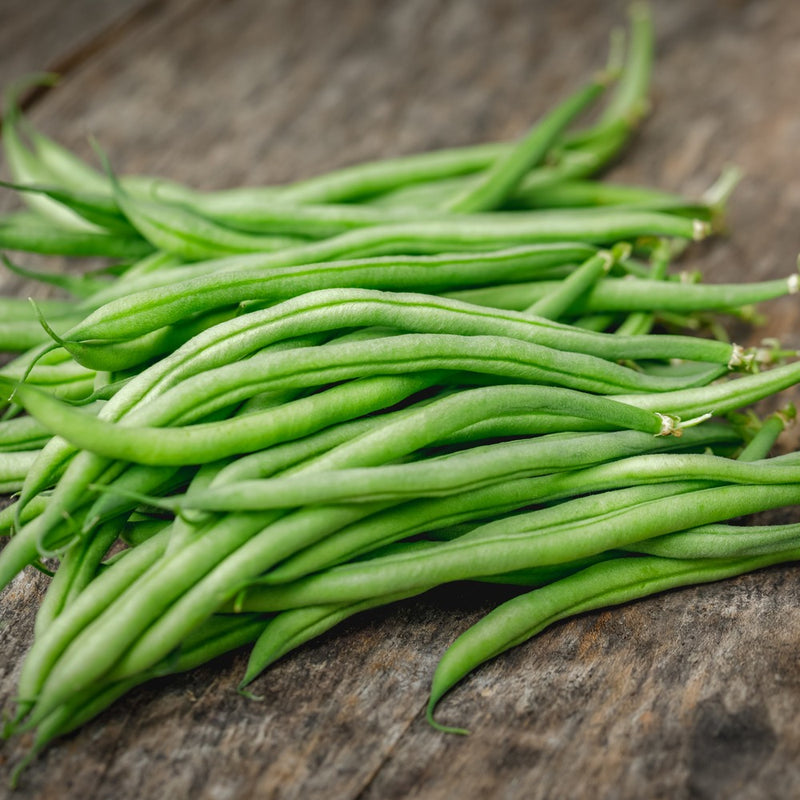 A pile of freshly picked, slender green French filet beans with pale stem ends, scattered on a weathered wooden surface.
