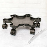 Black star-shaped plastic planter mover base with five scalloped indents and locking caster wheels at each point, shown beside a clear plastic support rod on a light surface.
