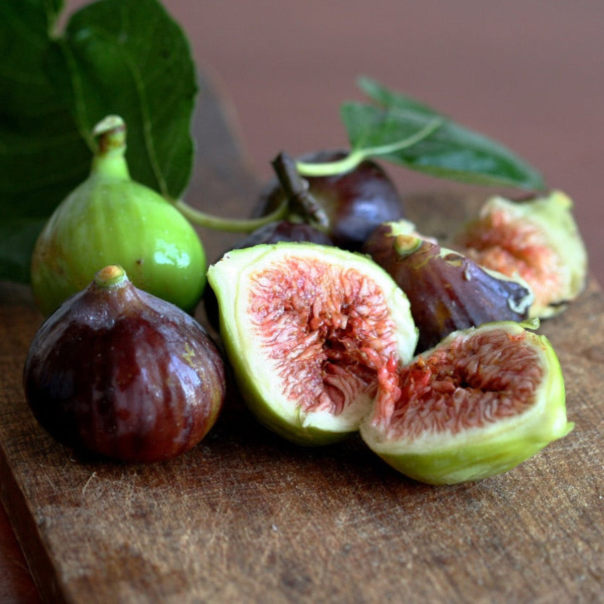 Whole and halved ripe Little Miss Figgy fruits on a wooden surface.