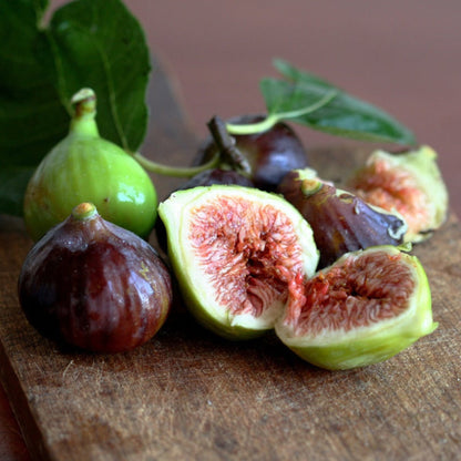 Whole and halved ripe Little Miss Figgy fruits on a wooden surface.
