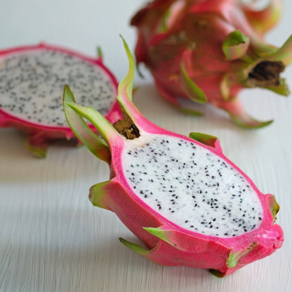 Halved white dragon fruit with bright pink skin and seed-speckled white flesh.