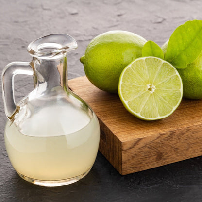 Glass pitcher of lime juice next to halved and whole Persian 'Bearss' limes.