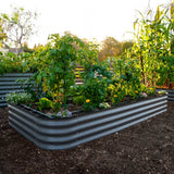 A slate gray metal raised garden bed filled with green plants and vegetables, shown in an outdoor garden setting with mulch and other garden beds in the background.