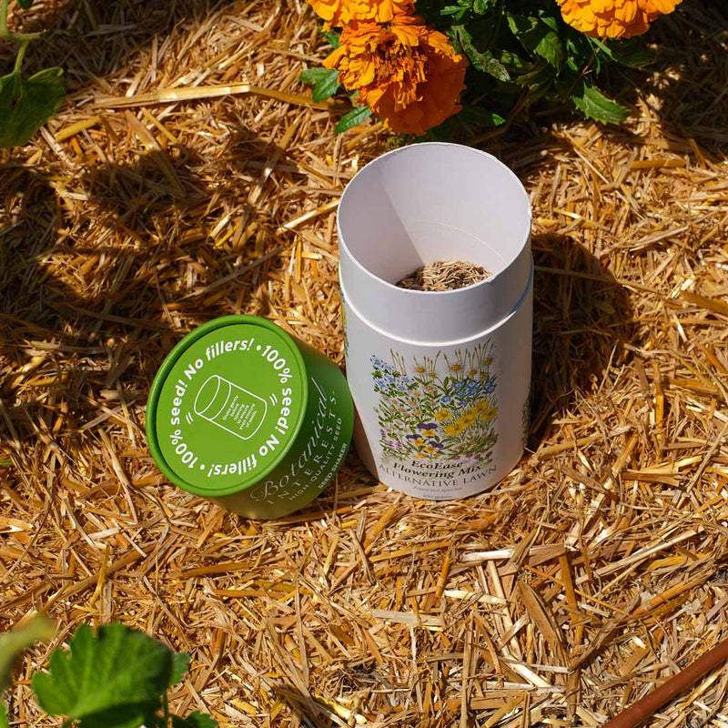 Opened EcoEase Flowering Mix Alternative Lawn Seed Shaker container on a straw background with flowers in the background