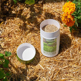 Opened EcoEase Microclover and Fescue Mix Alternative Lawn Seed Shaker filled with seeds on straw with flowers in the background