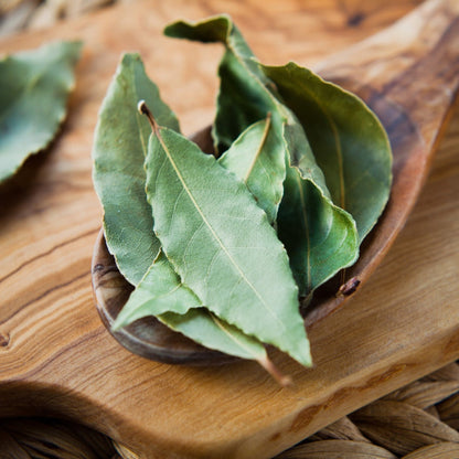 Dried bay leaves in a wooden spoon on a wooden board.